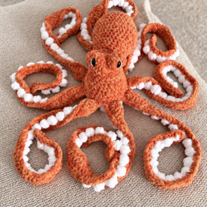 Juniper the Bloom Spirit, a coral-pink crocheted dragon with a yellow flower on her forehead