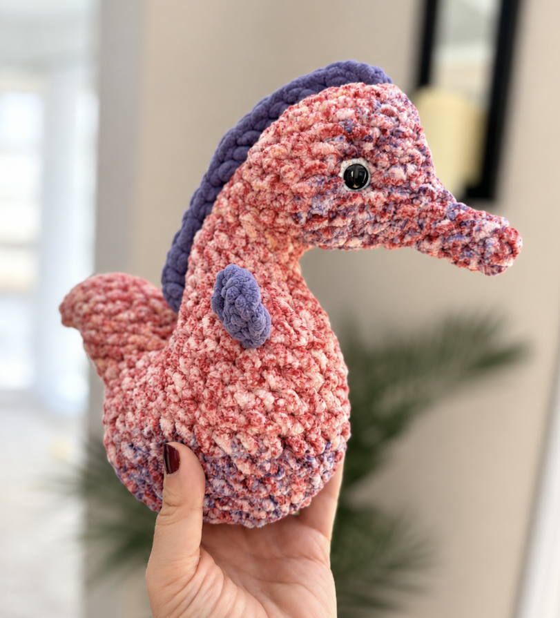 A dusty-pink crocheted pig with big floppy ears, held up in a sunny room