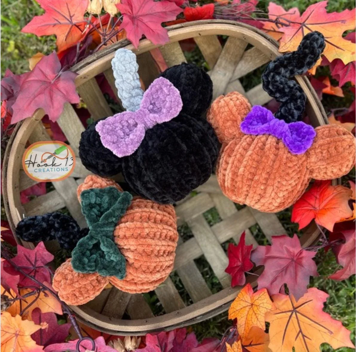 Three crocheted mouse-eared pumpkins in a slatted basket among autumn leaves