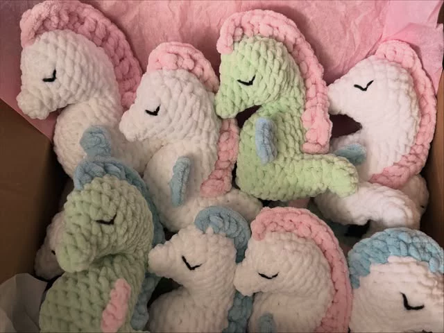 A box of crocheted seahorses in white, pink, mint and blue with stitched sleeping eyes, made for the bereavement boxes